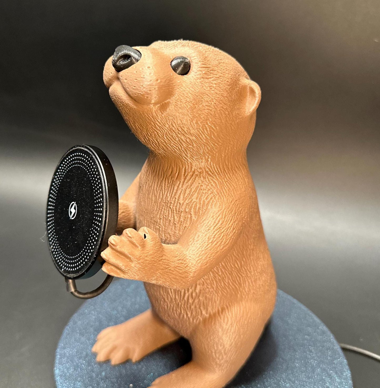 A cute gray otter figure holding a magnetic phone charger dock. Functional and adorable addition to any tech setup.β