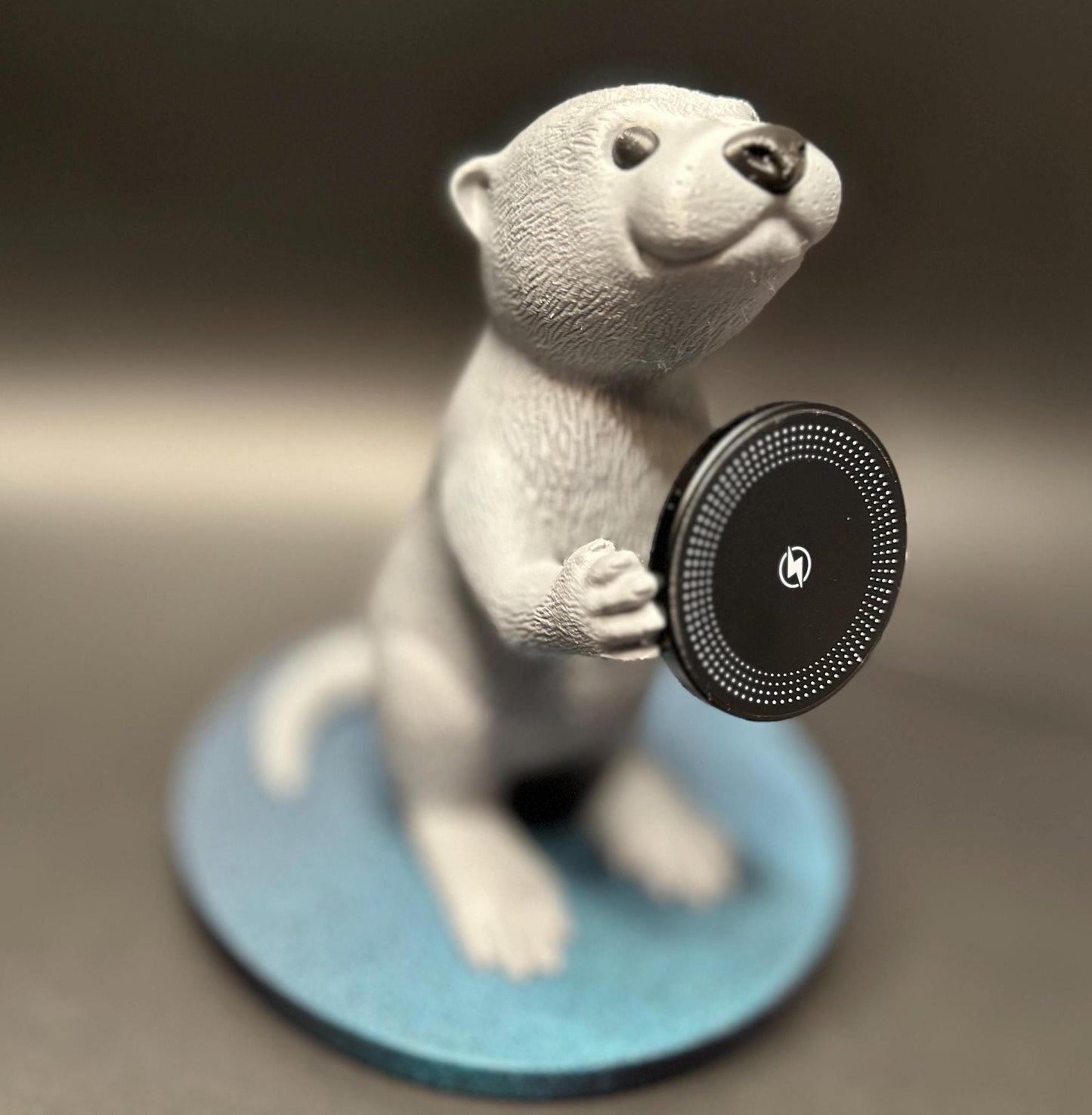 A cute gray otter figure holding a magnetic phone charger dock. Functional and adorable addition to any tech setup.β