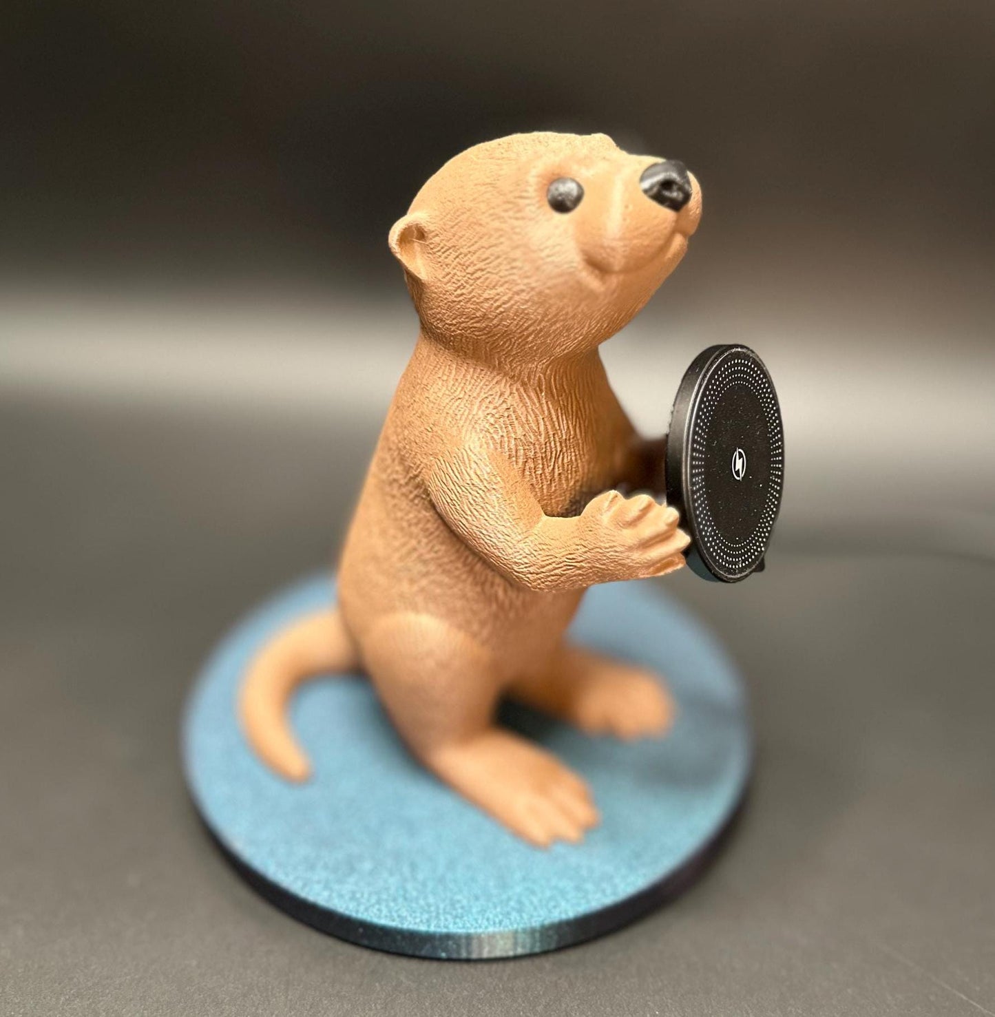 A cute gray otter figure holding a magnetic phone charger dock. Functional and adorable addition to any tech setup.β