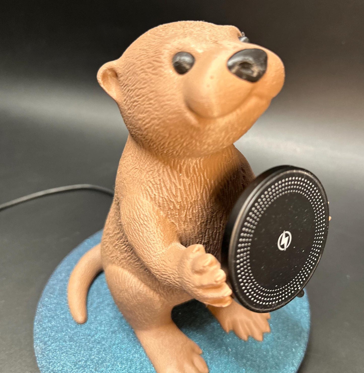 A cute gray otter figure holding a magnetic phone charger dock. Functional and adorable addition to any tech setup.β