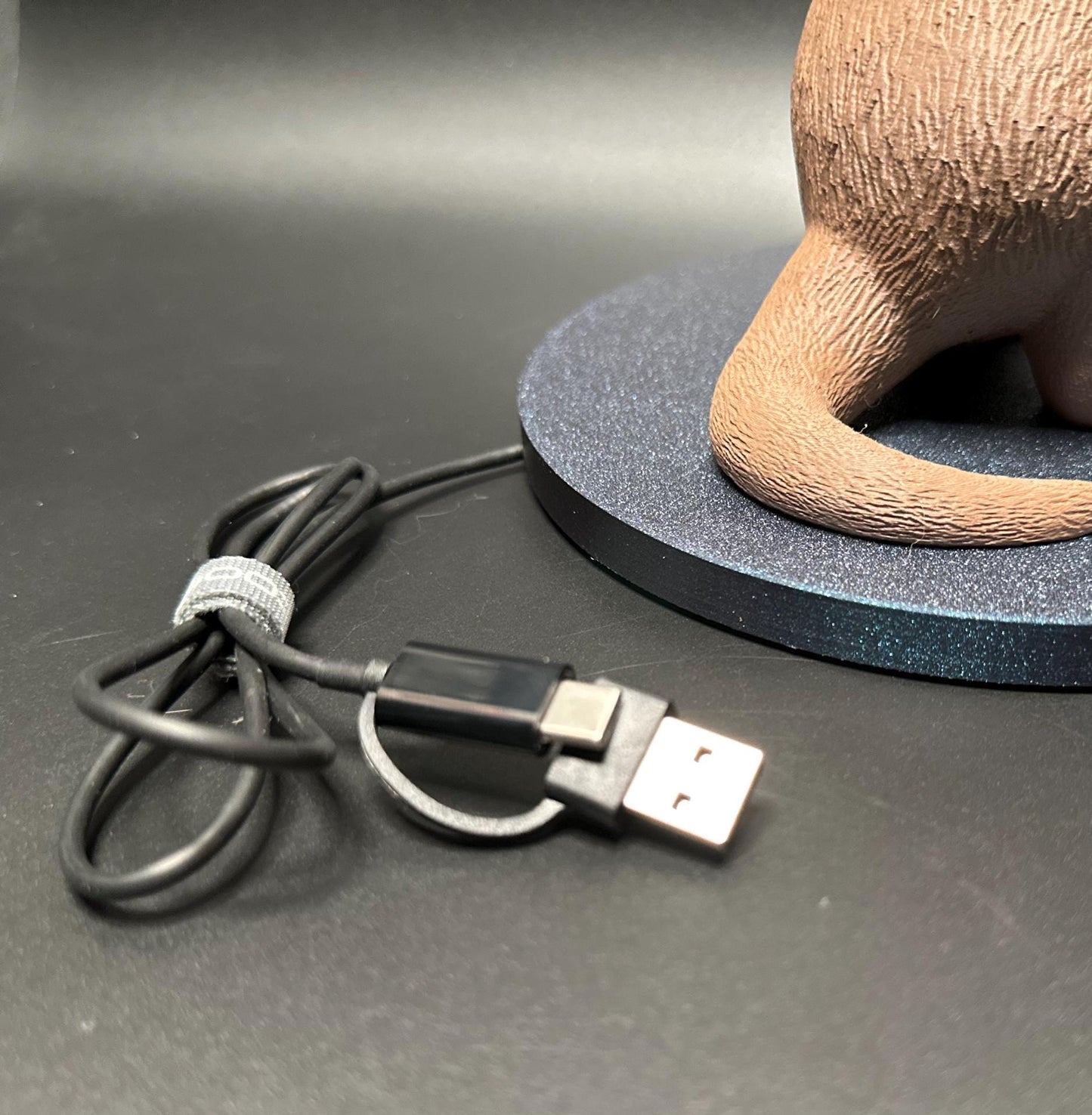 A cute gray otter figure holding a magnetic phone charger dock. Functional and adorable addition to any tech setup.β