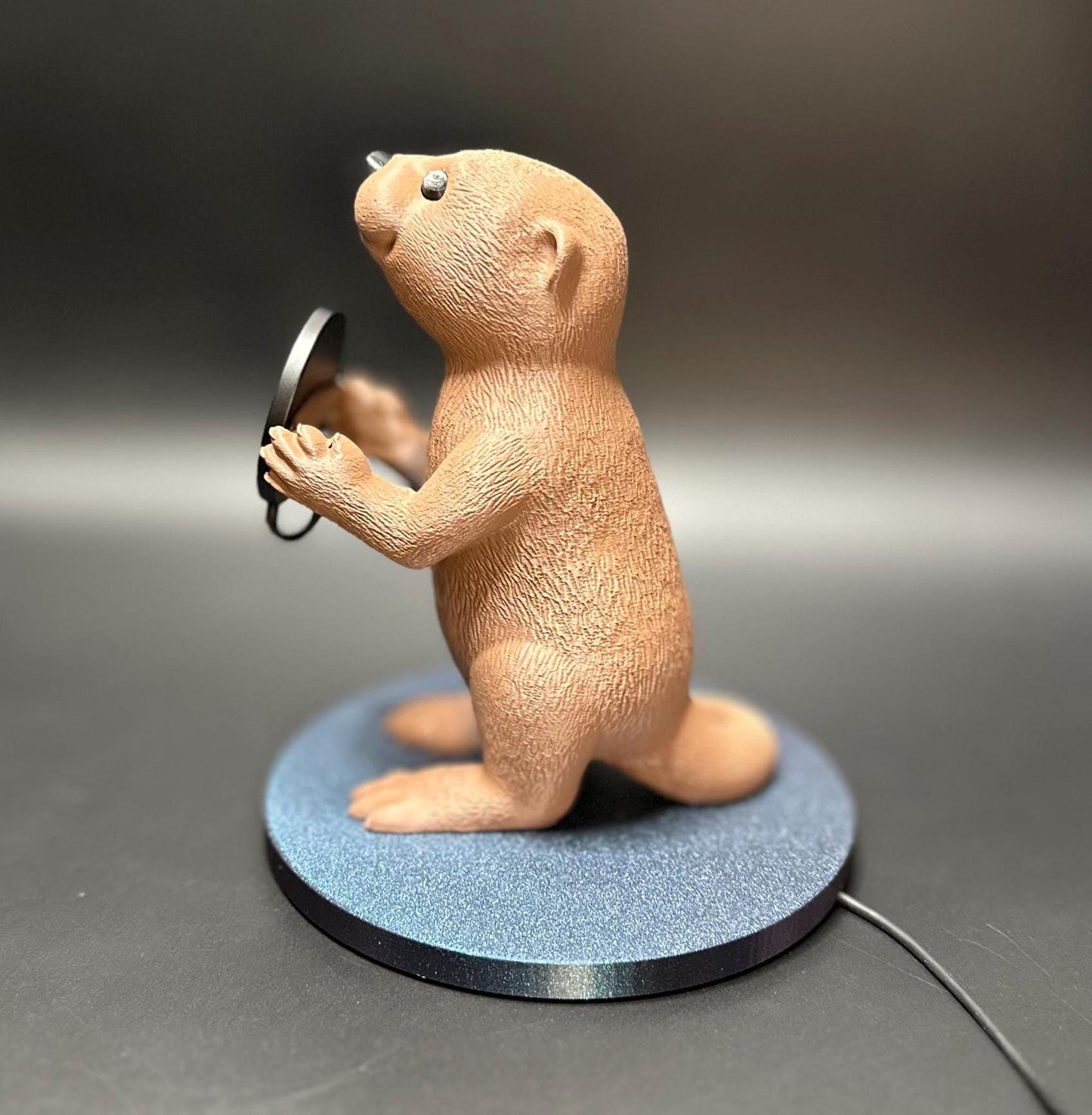 A cute gray otter figure holding a magnetic phone charger dock. Functional and adorable addition to any tech setup.β